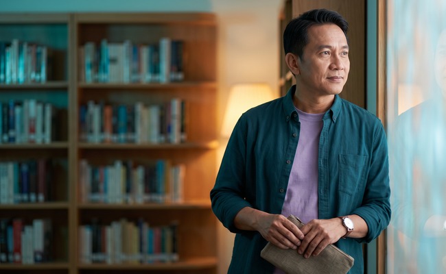 Person pausing in a quiet library alcove with a small pouch.