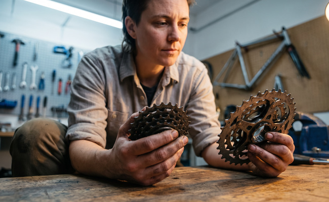 Adult comparing two unmarked bicycle gear assemblies at a workshop bench.