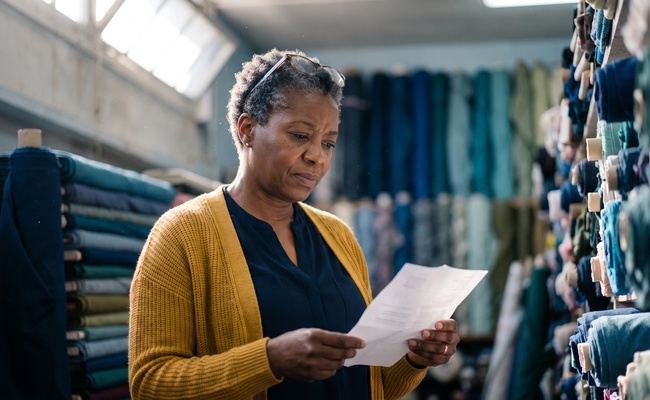 Woman in a fabric store aisle reading a collection notice with a balance far higher than she remembered.