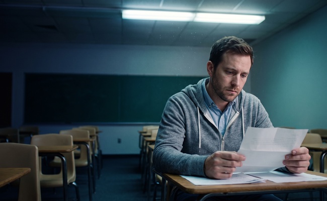 Man alone in an empty classroom reading a collection letter after hours.