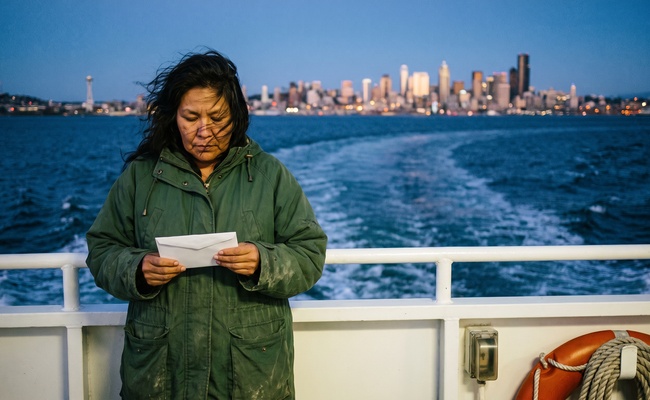 Woman at a ferry deck rail at dusk holding a sealed envelope she has not opened.
