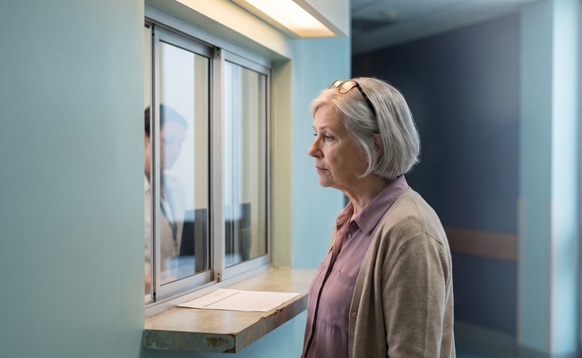 Older woman waiting at a medical records request window to obtain proof of payment.
