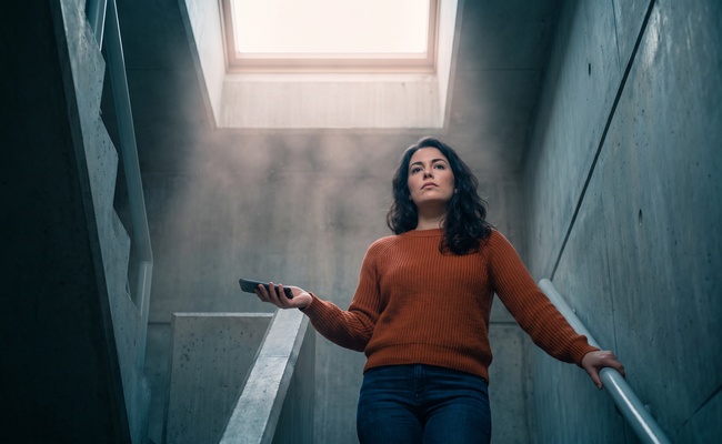 Young woman on a stairwell landing holding her phone face down instead of answering.