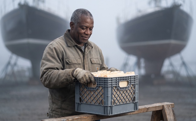 The same man from the opening stands in morning fog looking with quiet satisfaction at a crate of sorted and labeled folders.