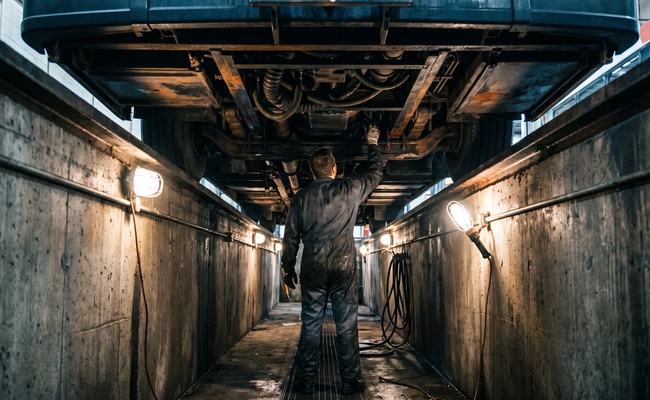A mechanic works upward from inside a maintenance pit, reaching into machinery from below the way a claim for money already taken works from underneath a completed garnishment.