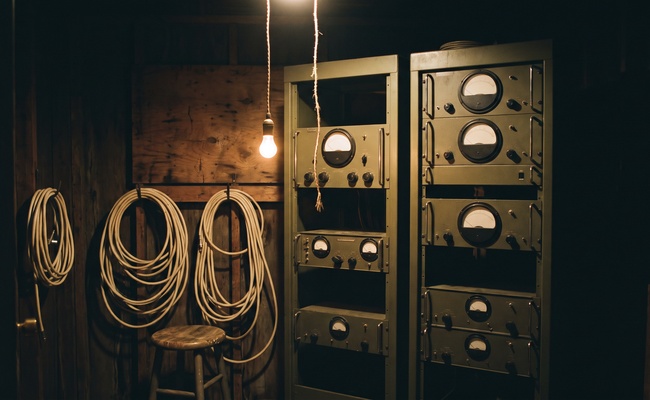 An old transmitter shack lit by one bulb, standing for the bills that keep running after creditors take money from a joint account.