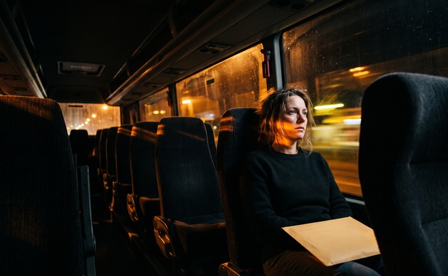 Passenger on an overnight coach holding a sealed envelope as sodium lights pass the windows