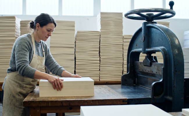 Print shop bindery with stacked paper seen edge on beside a cast iron guillotine cutter