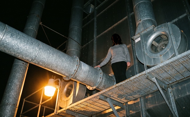 Worker on a steel catwalk among galvanised ducting under a sodium work light