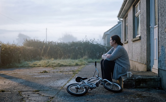 Woman sitting on a back step at dawn beside a child's bicycle laid on the path