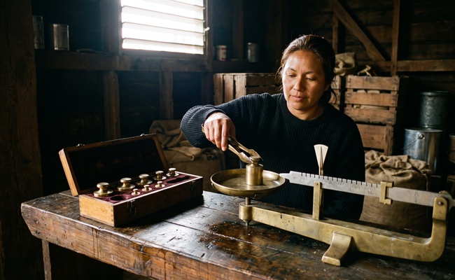 A brass beam balance and a case of plain brass weights on a timber bench