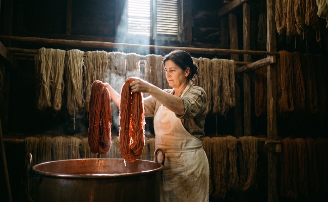 A dyer comparing two wool skeins of slightly different depth above a copper vat