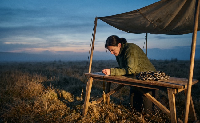 A surveyor adjusting a plumb line at a folding field bench at dusk