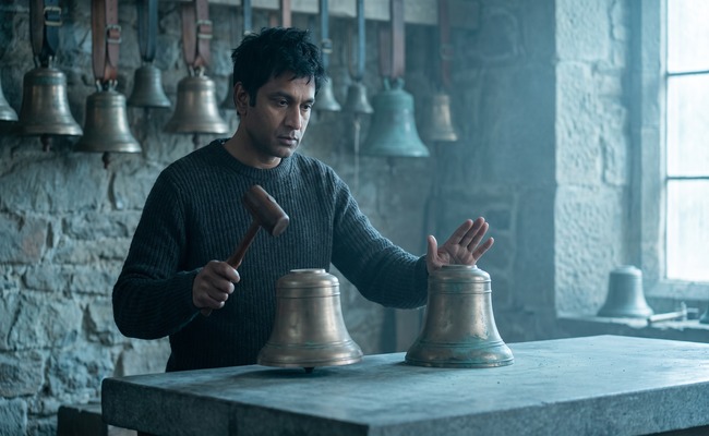 A bell tuner strikes one bronze bell with a mallet while holding an identical bell silent.
