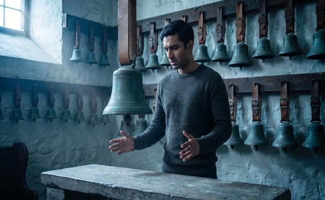 A person looks down at a bronze bell swinging faintly while holding both hands open.